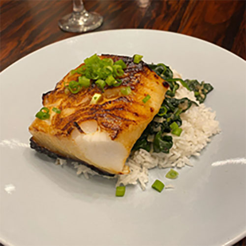 Top view of a portion of fish on a bed of rice with green onion